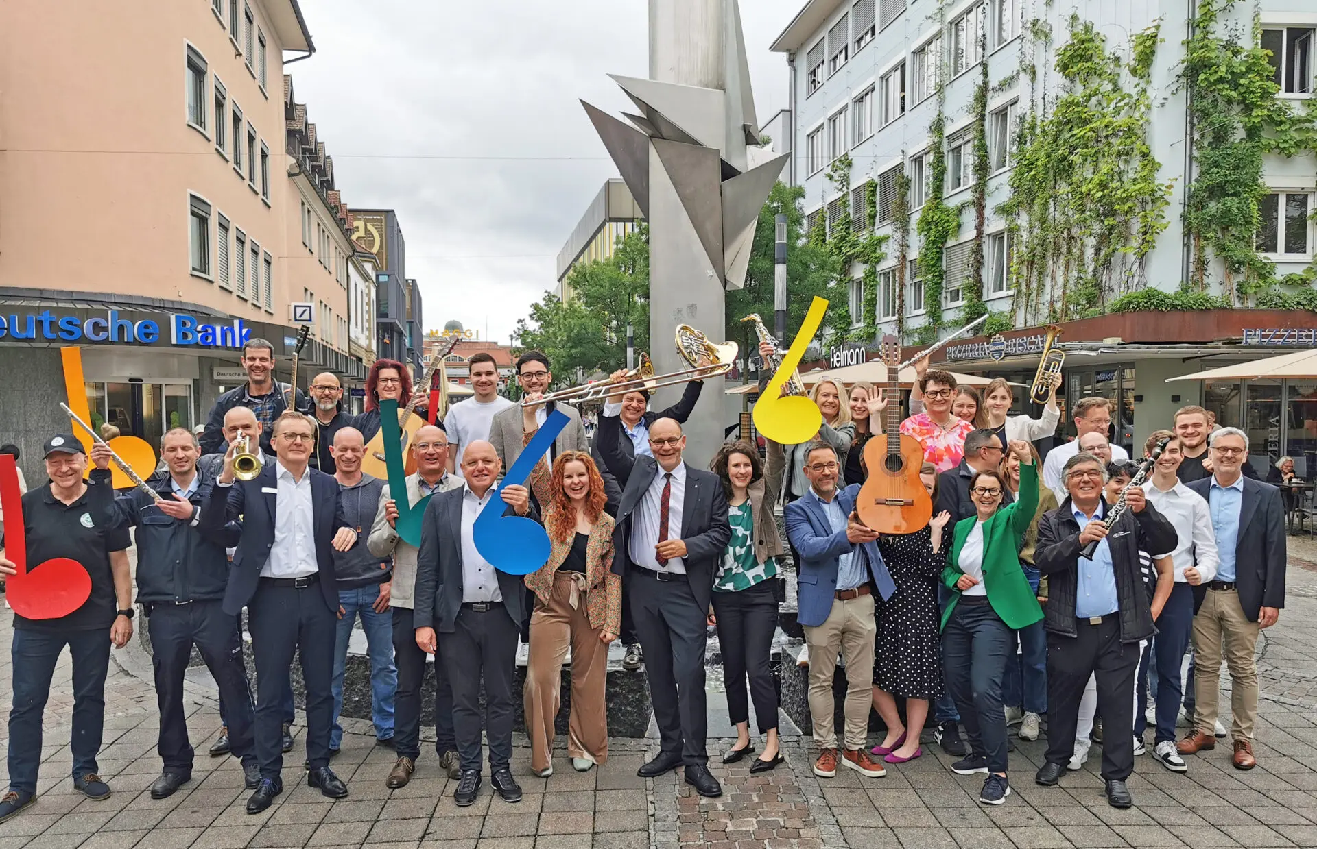 Fröhliche Organisatoren und Sponsoren des Stadtfests Singen und des Landes-Musik-Festivals, die bei einem Gruppenbild Instrumente und Notenköpfe in die Höhe halten.
