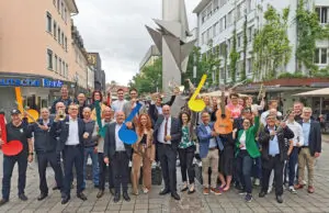 Fröhliche Organisatoren und Sponsoren des Stadtfests Singen und des Landes-Musik-Festivals, die bei einem Gruppenbild Instrumente und Notenköpfe in die Höhe halten.